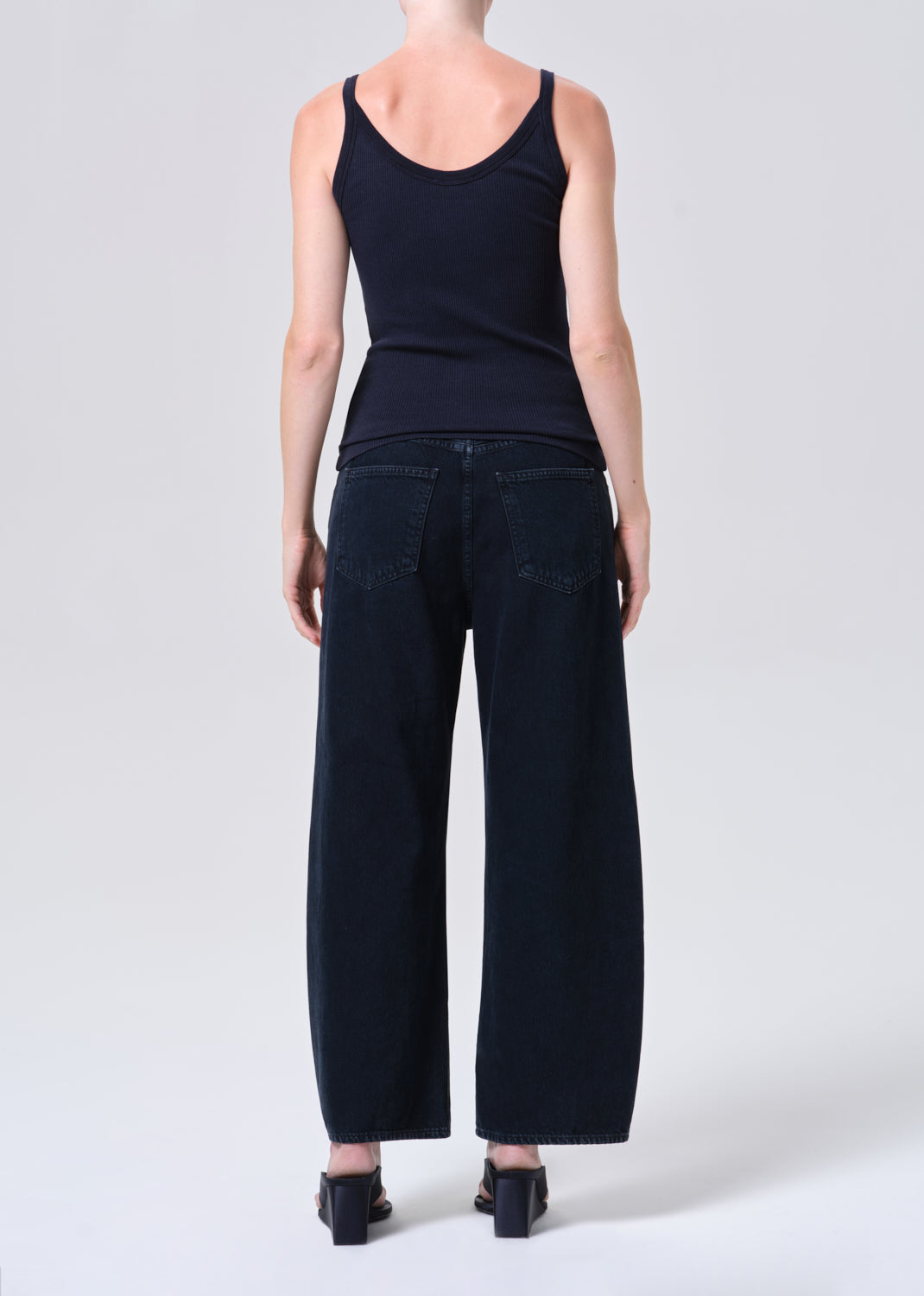 Person wearing a black tank top and dark jeans on a white background