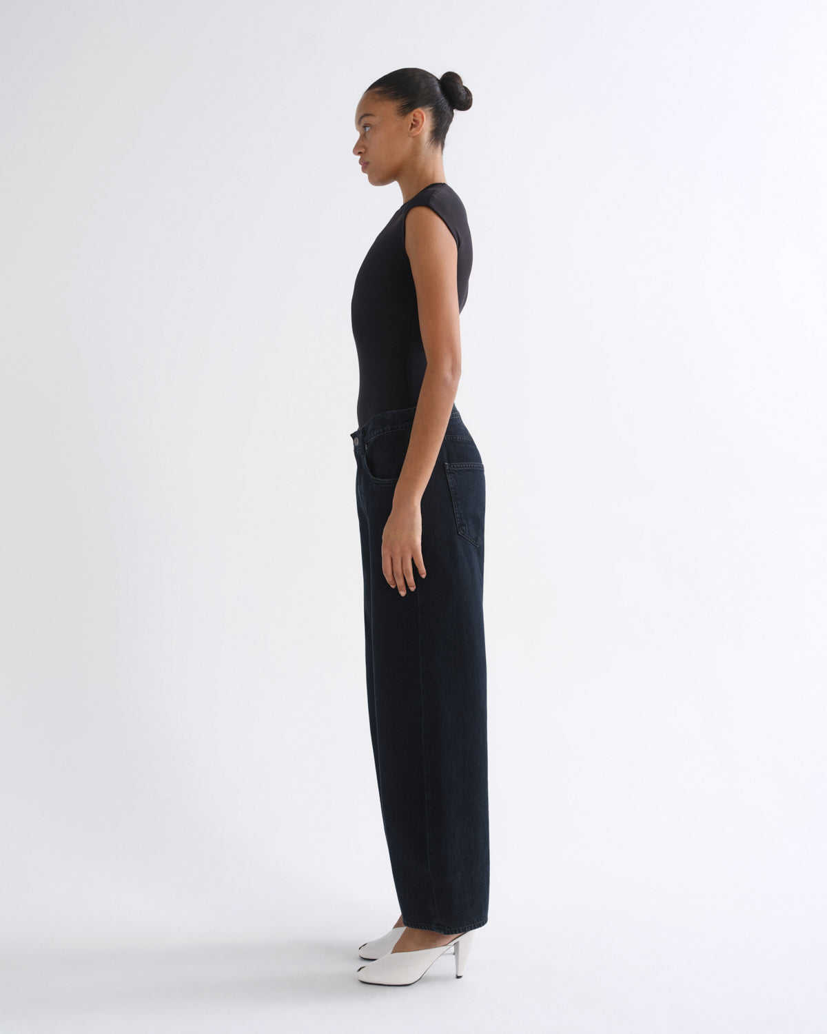A model shown from the side wearing a black short-sleeve top and dark wide-leg jeans against a plain white studio background.