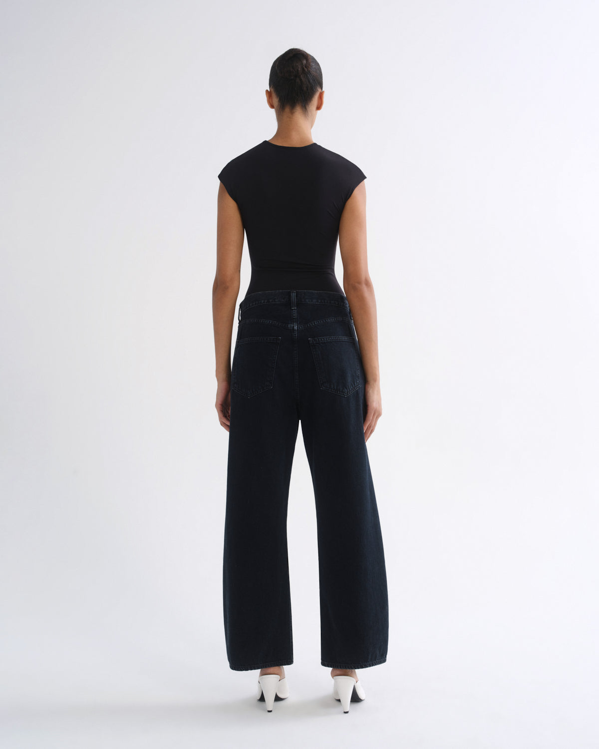 A model shown from the back wearing a black short-sleeve top and dark wide-leg jeans against a plain white studio background.