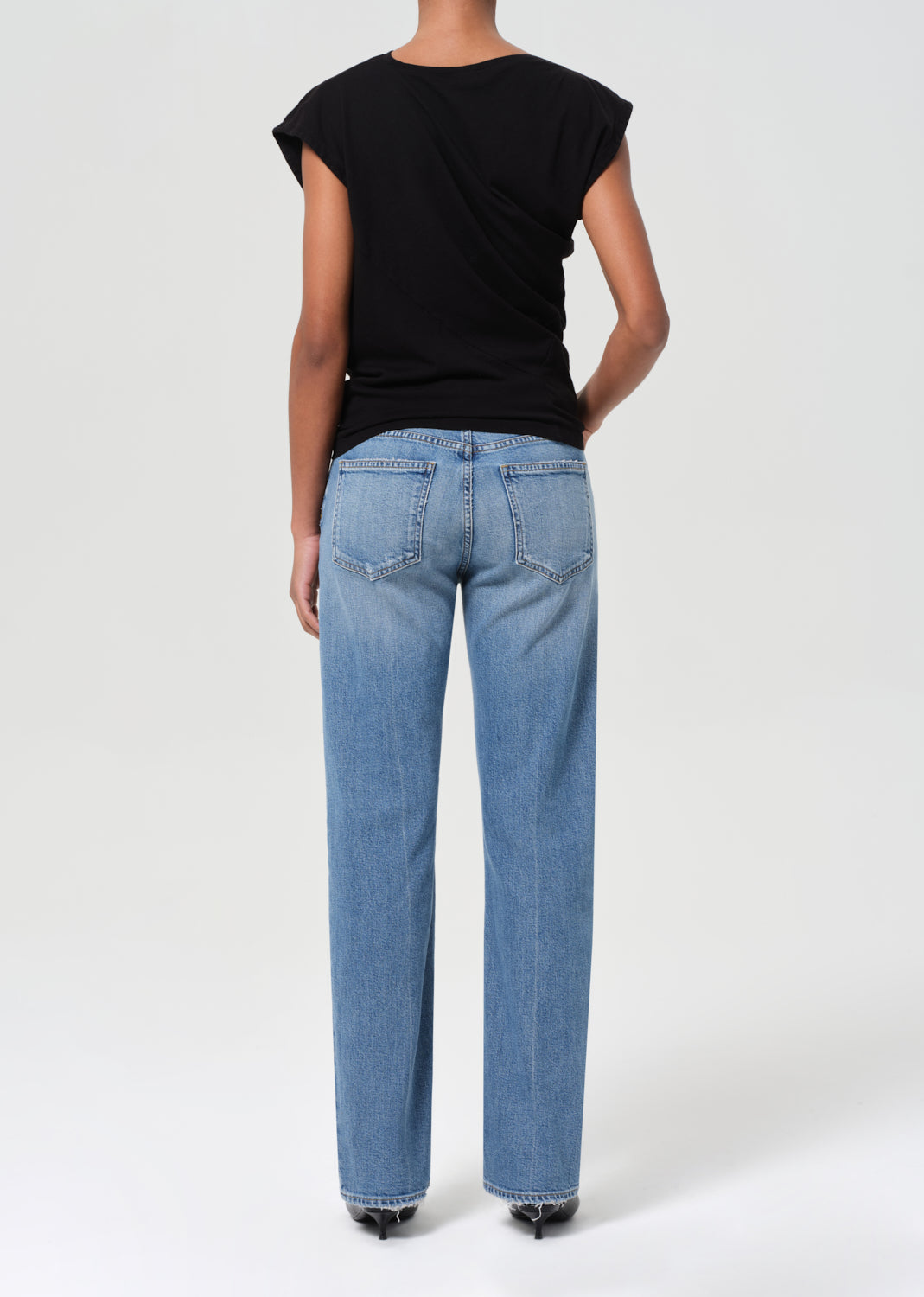 Person wearing blue jeans and a black top on a white background