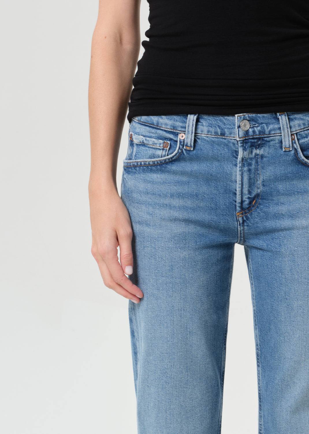 Person wearing blue jeans and a black top on a light gray background
