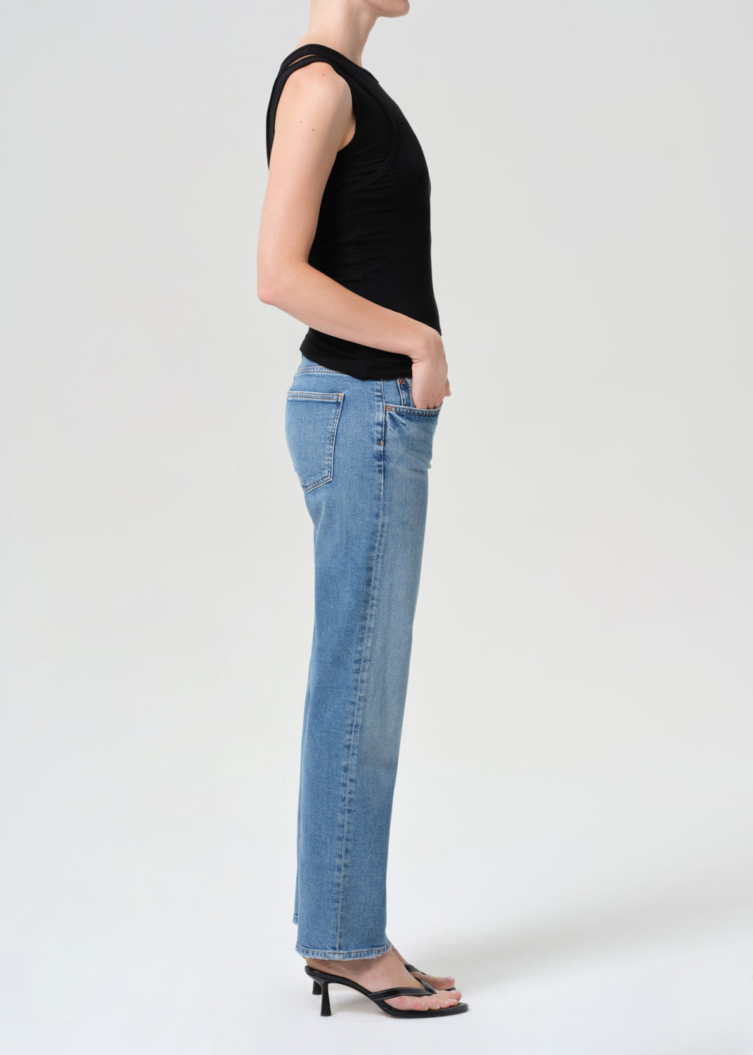 Person wearing a black sleeveless top and blue jeans on a white background