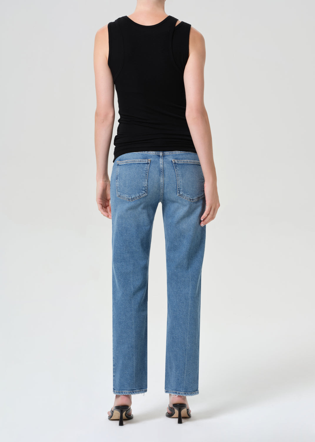 Person wearing a black sleeveless top and blue jeans on a white background