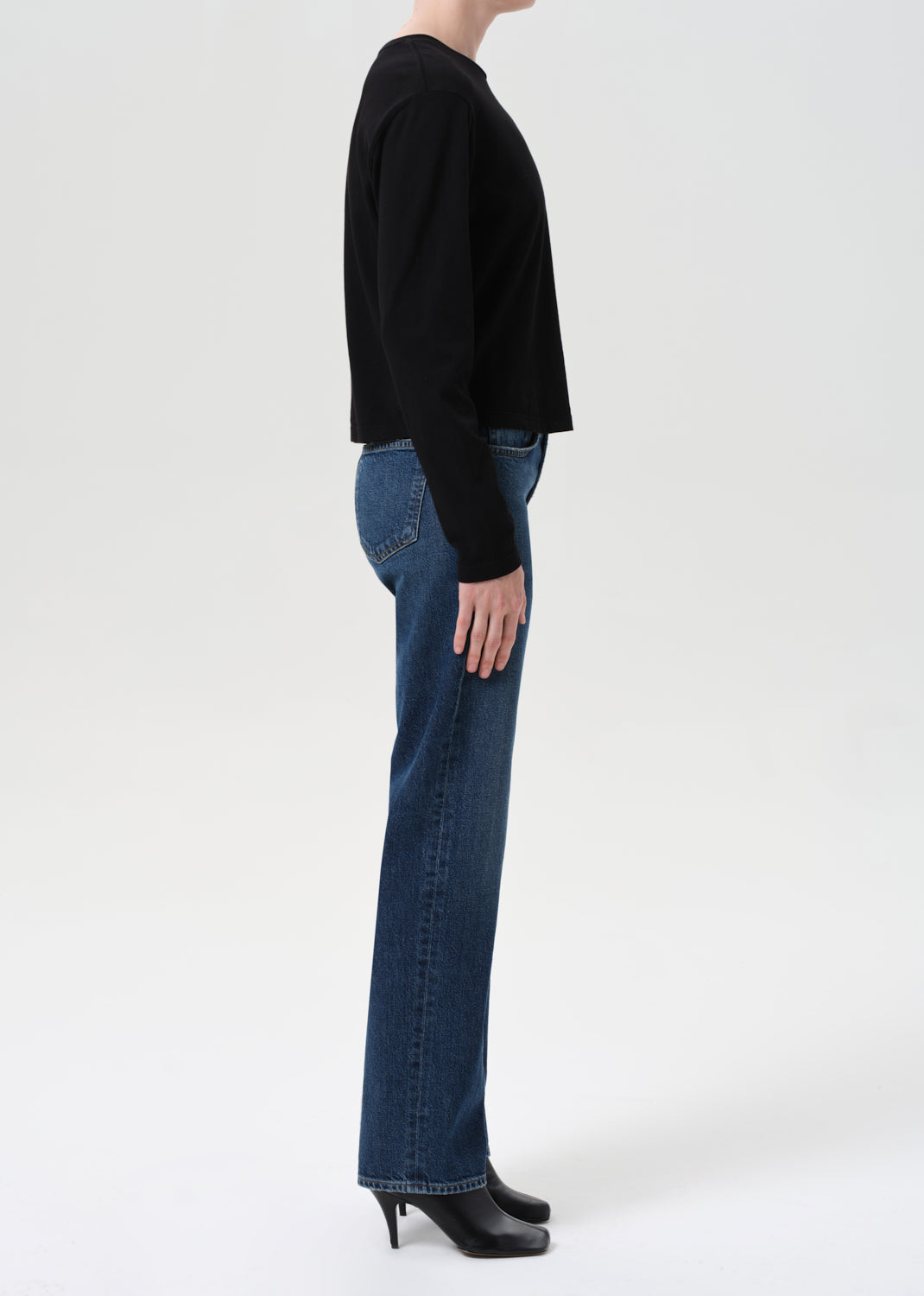 Person wearing a black long-sleeve top and blue jeans on a white background