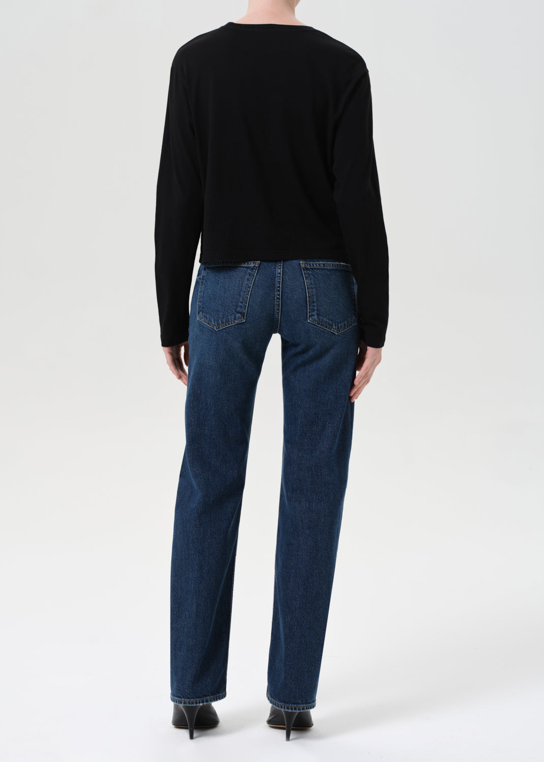 Person wearing a black sweater and blue jeans on a white background