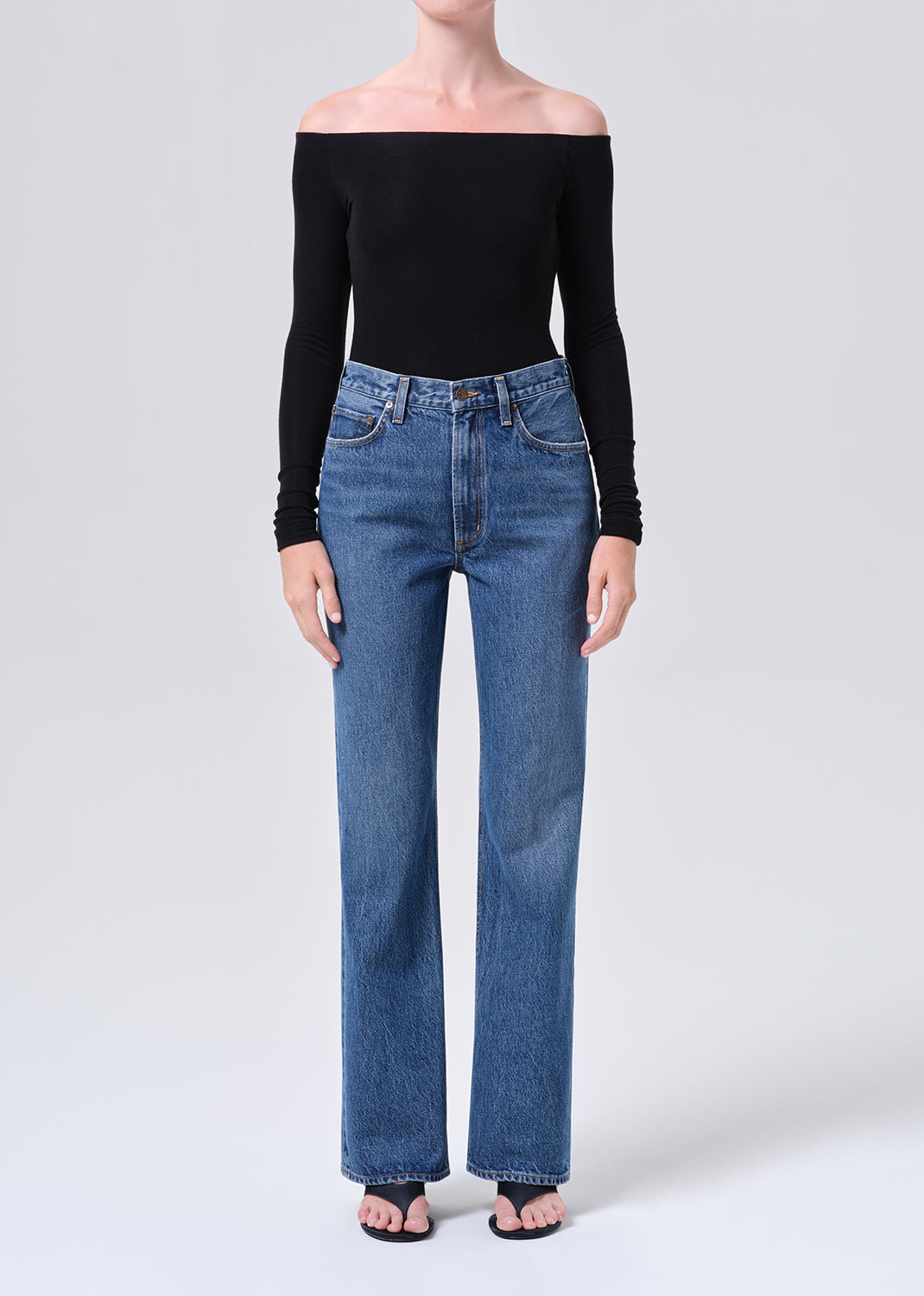 Person wearing a black off-shoulder top and blue jeans on a white background