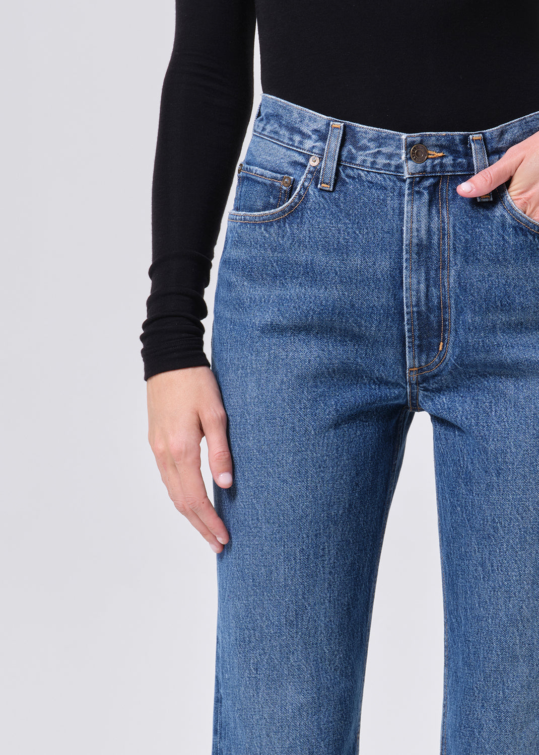 Person wearing blue jeans and a black long-sleeve shirt on a light gray background