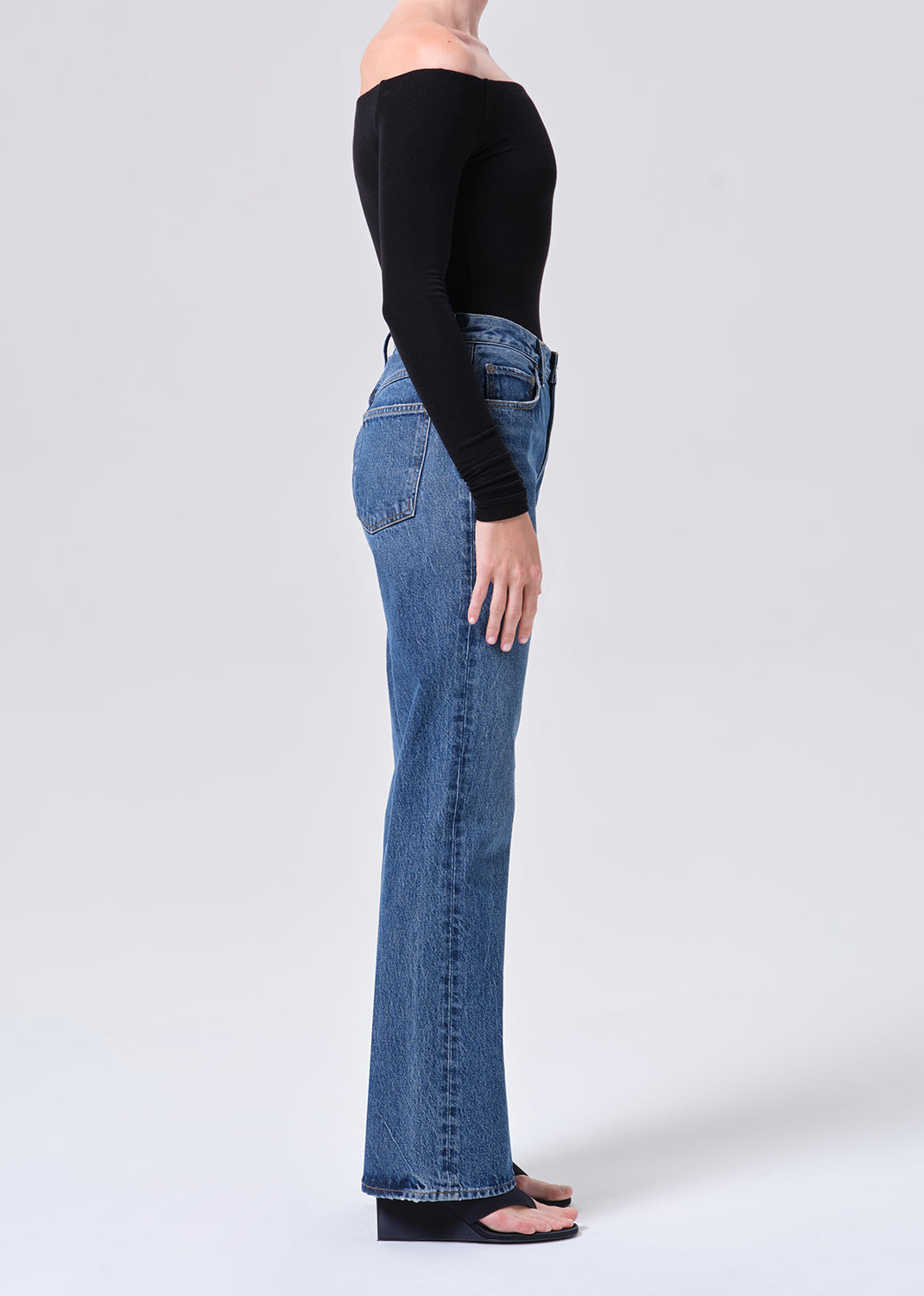 Person wearing blue jeans and a black top on a white background