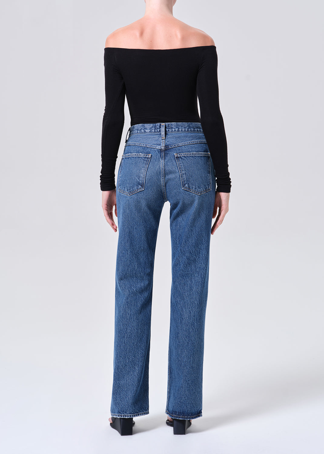 Person wearing blue jeans and a black off-shoulder top on a white background