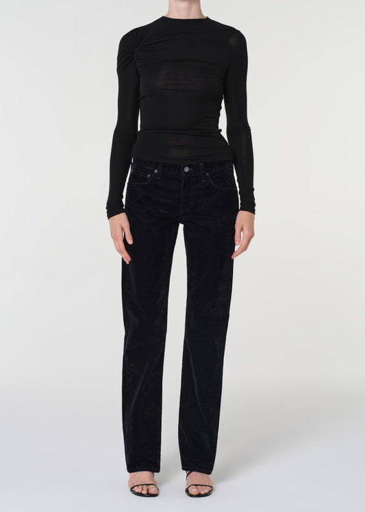 Person wearing a black long-sleeve top and blue velvet pants on a white background