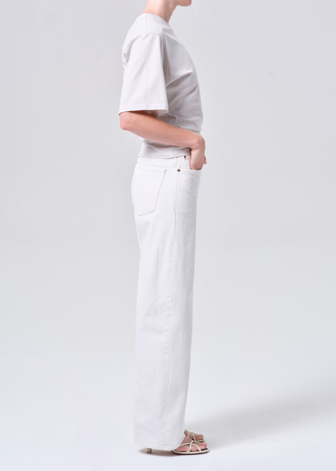 Person wearing a light gray shirt and white pants on a plain background