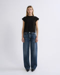 A model stands against a light gray studio background wearing a black short-sleeve crewneck top and dark blue wide-leg jeans.