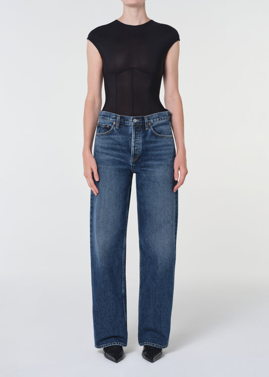 Person wearing a black top and blue jeans on a white background