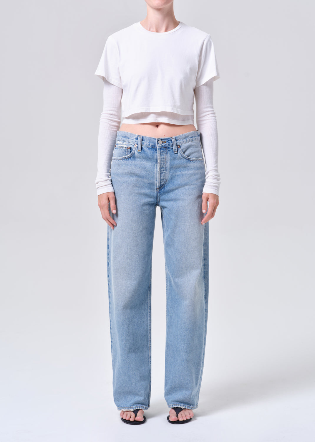 Person wearing light blue jeans and a white cropped top on a plain background