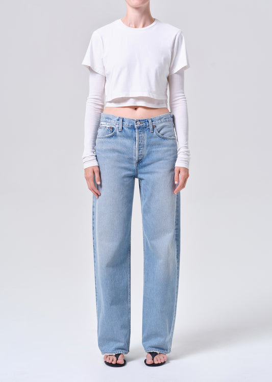 Person wearing light blue jeans and a white cropped top on a plain background