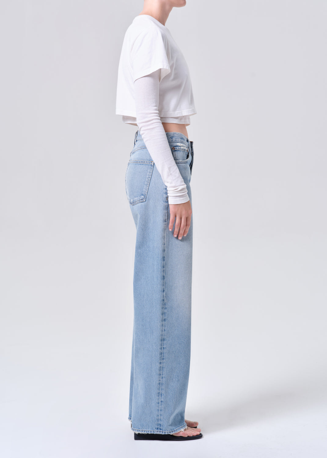 Person wearing light blue jeans and a white crop top on a plain background