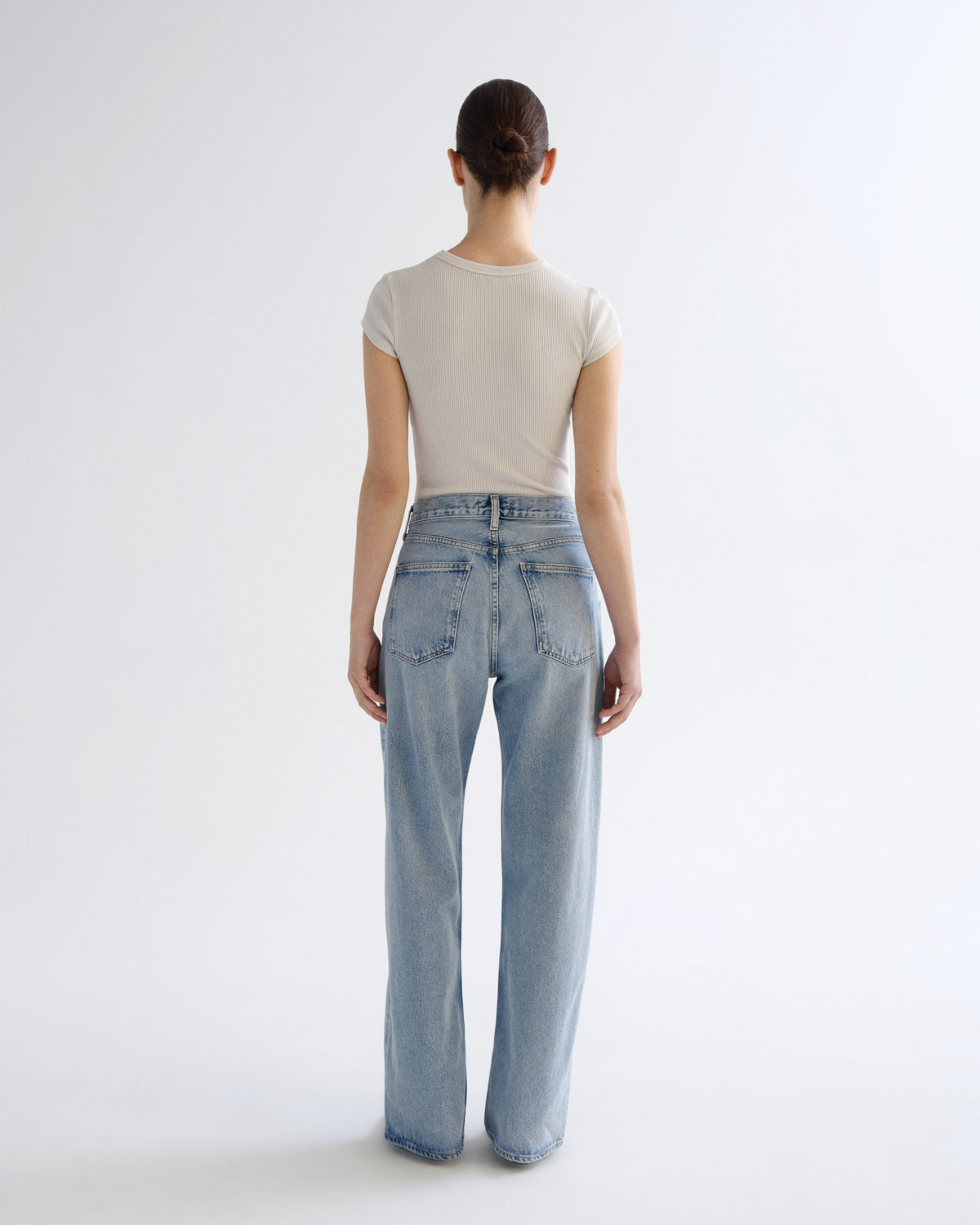 A model shown from the back wearing a light beige short-sleeve t-shirt and light-wash blue wide-leg jeans against a plain white studio background.