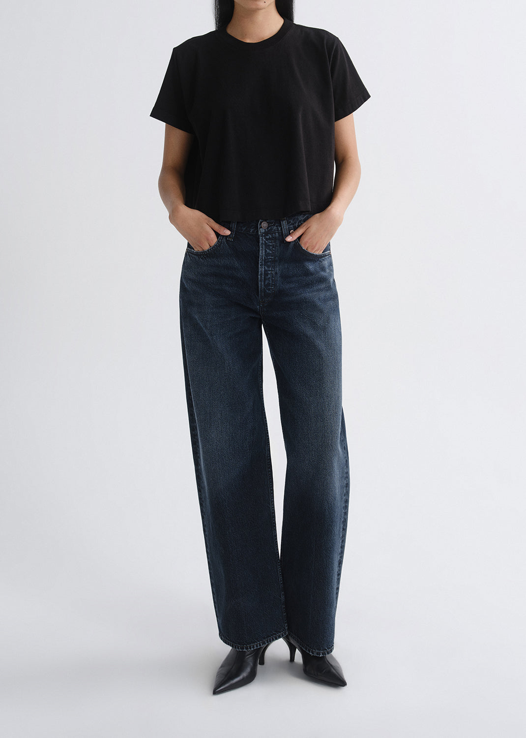 Person wearing a black short sleeve crewneck tee with dark wash wide leg jeans on a grey background