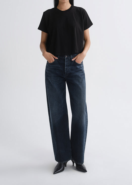 Person wearing a black short sleeve crewneck tee with dark wash wide leg jeans on a grey background