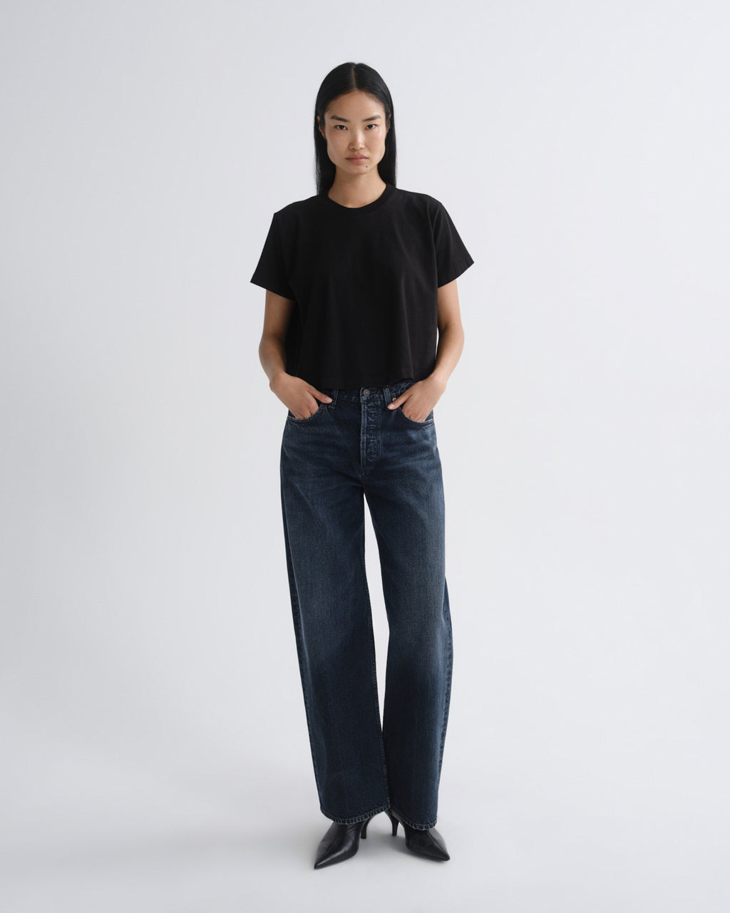 Person wearing a black t-shirt and dark jeans on a white background