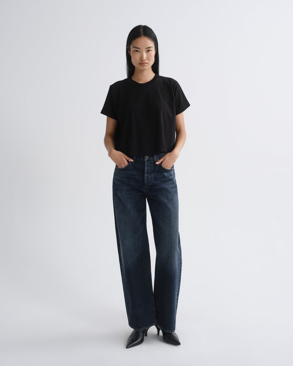 Person wearing a black t-shirt and dark jeans on a white background