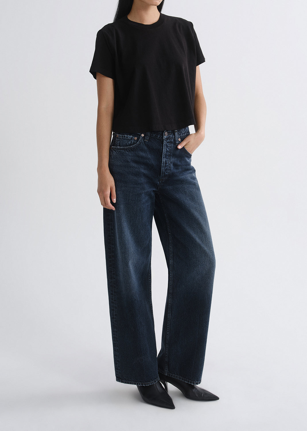 Person wearing a black short sleeve crewneck tee with dark wash wide leg jeans on a grey background