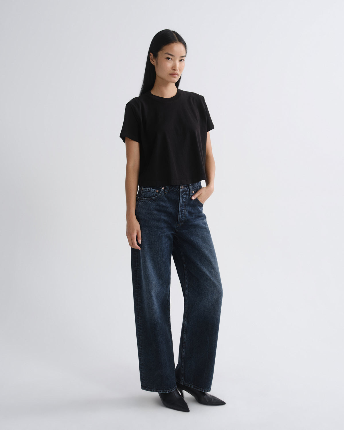 Person wearing a black t-shirt and dark blue jeans on a white background