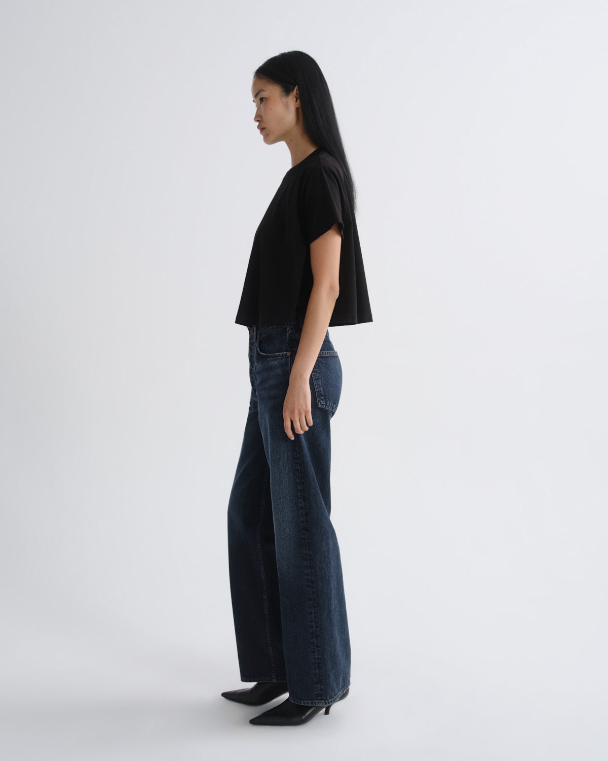 Person wearing a black top and dark blue jeans on a white background
