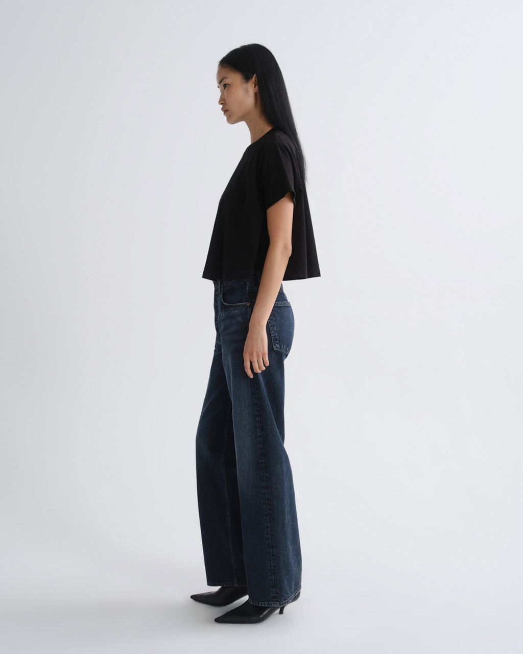 Person wearing a black top and dark blue jeans on a white background