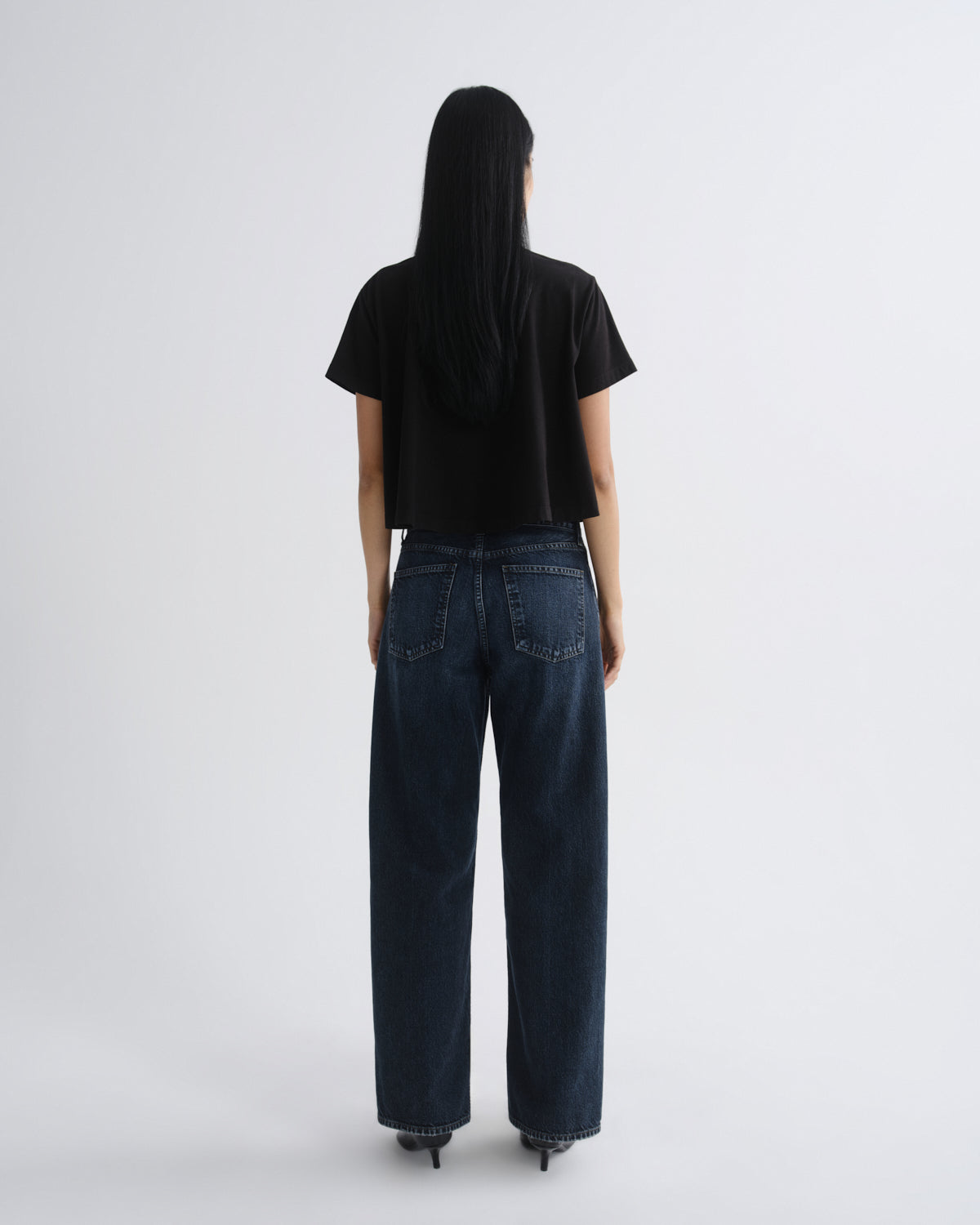 Person wearing a black t-shirt and dark blue jeans on a white background