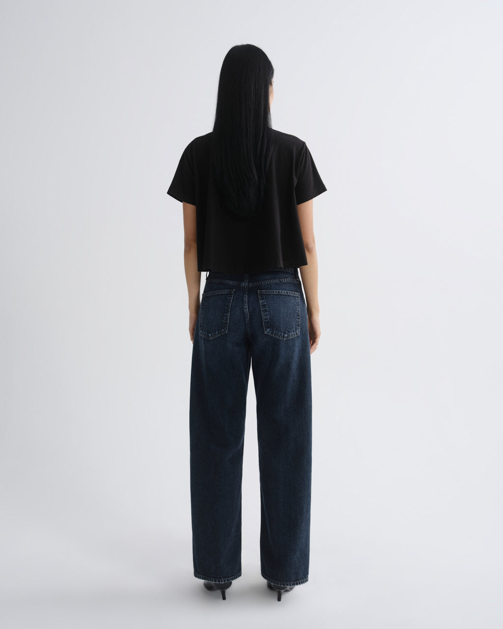 Person wearing a black t-shirt and dark blue jeans on a white background