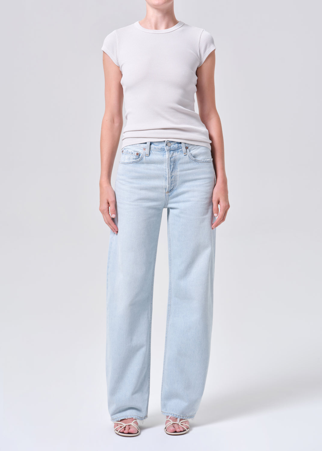 Person wearing light blue jeans and a white top on a plain background