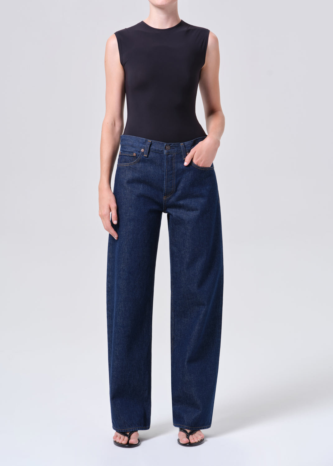 Person wearing a black sleeveless top and blue jeans on a white background