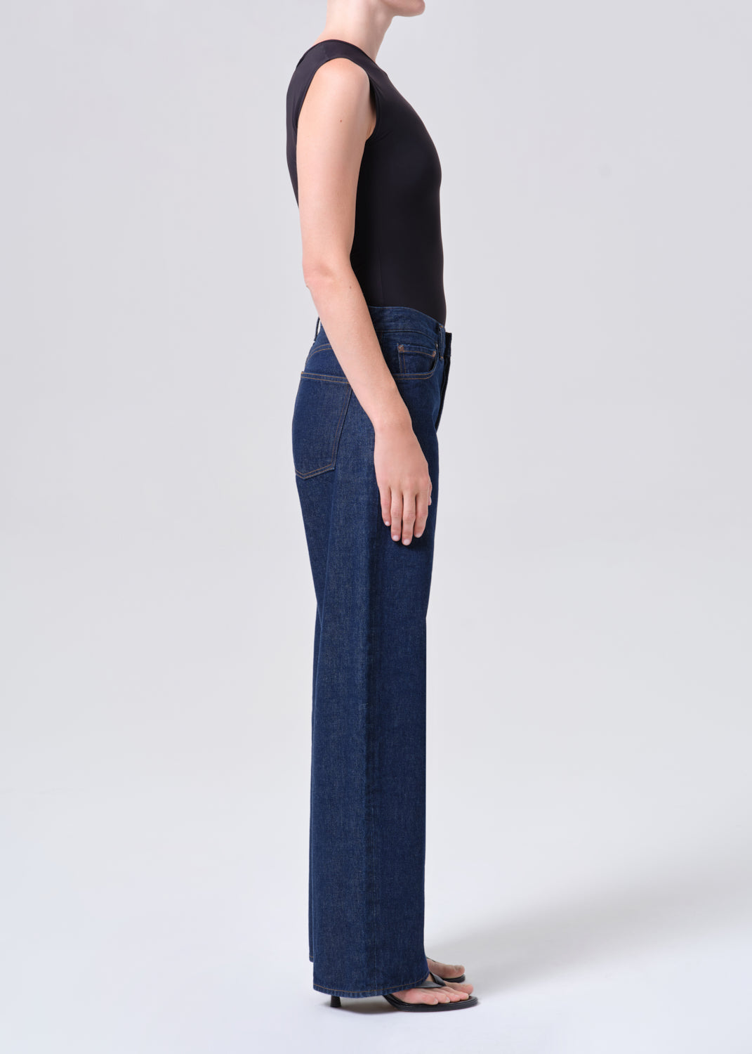 Person wearing dark blue jeans and a black sleeveless top on a white background