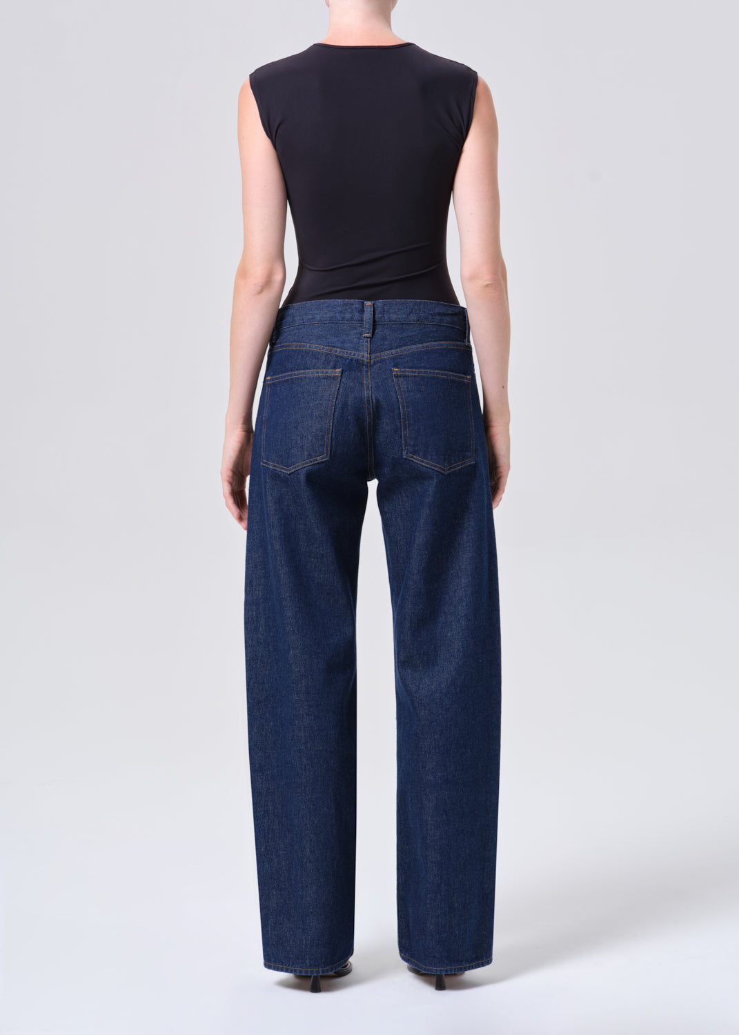 Person wearing blue jeans and a black top on a white background