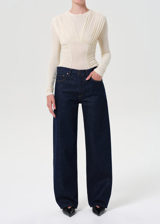 Person wearing a cream long-sleeve top and dark blue jeans on a white background