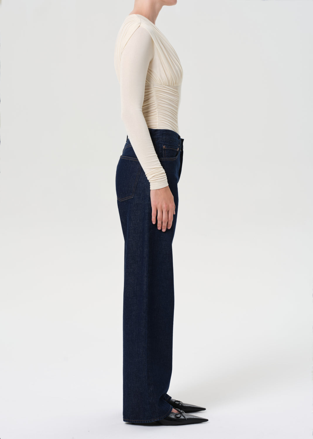 Person wearing a cream long-sleeve top and dark blue jeans on a white background