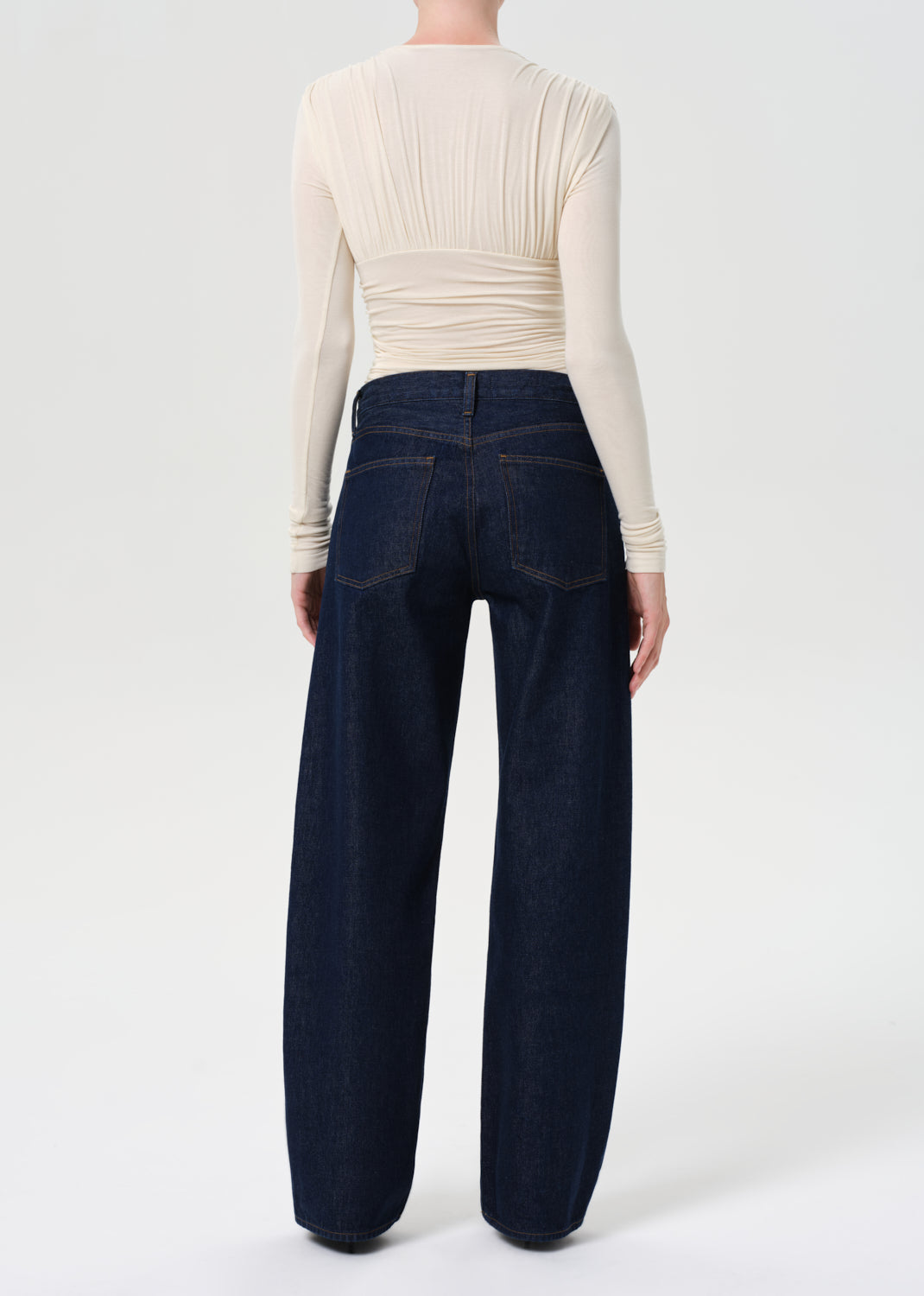 Person wearing a cream long-sleeve top and dark blue wide-leg pants on a white background