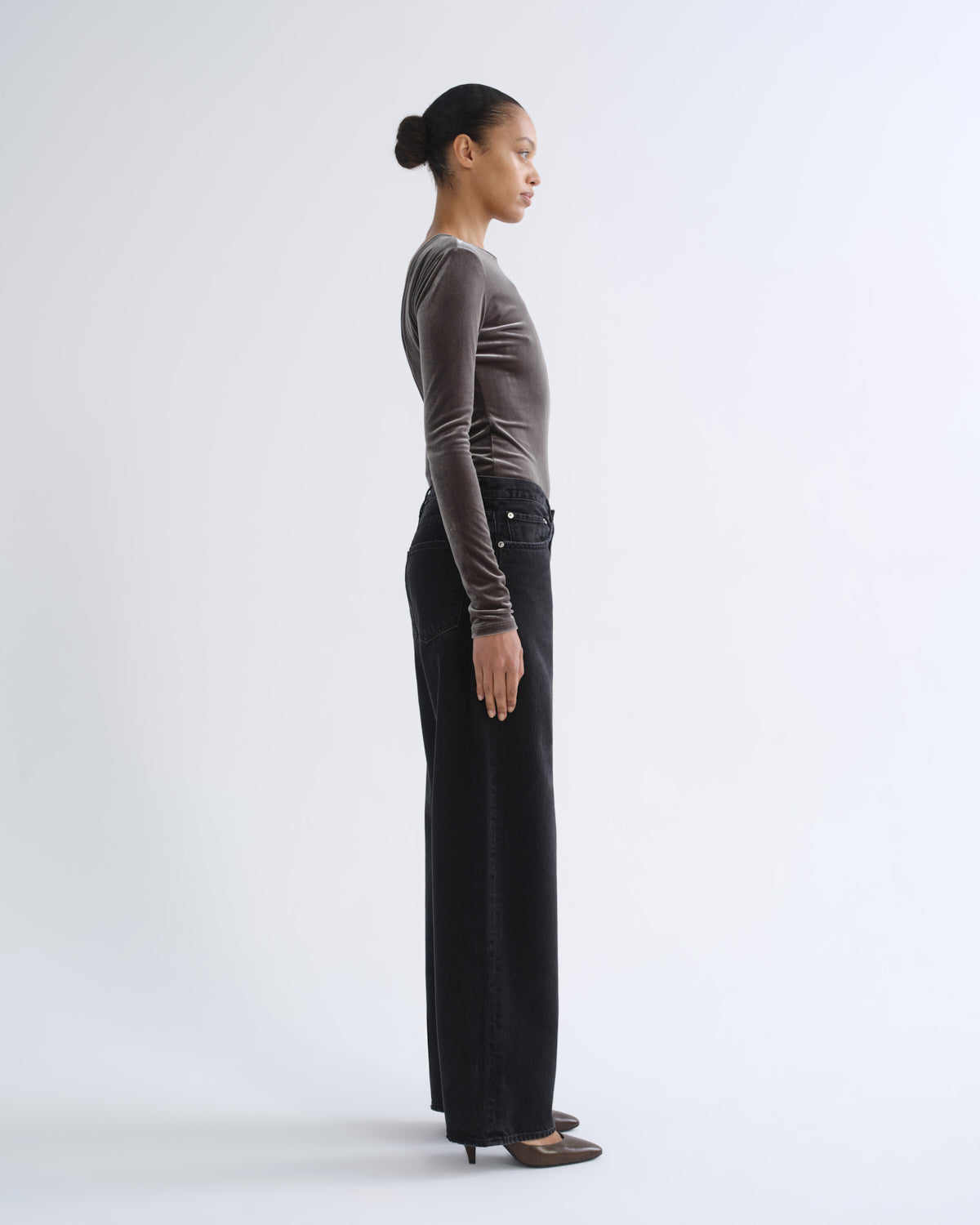 Person wearing brown long sleeve top and black jeans, side view