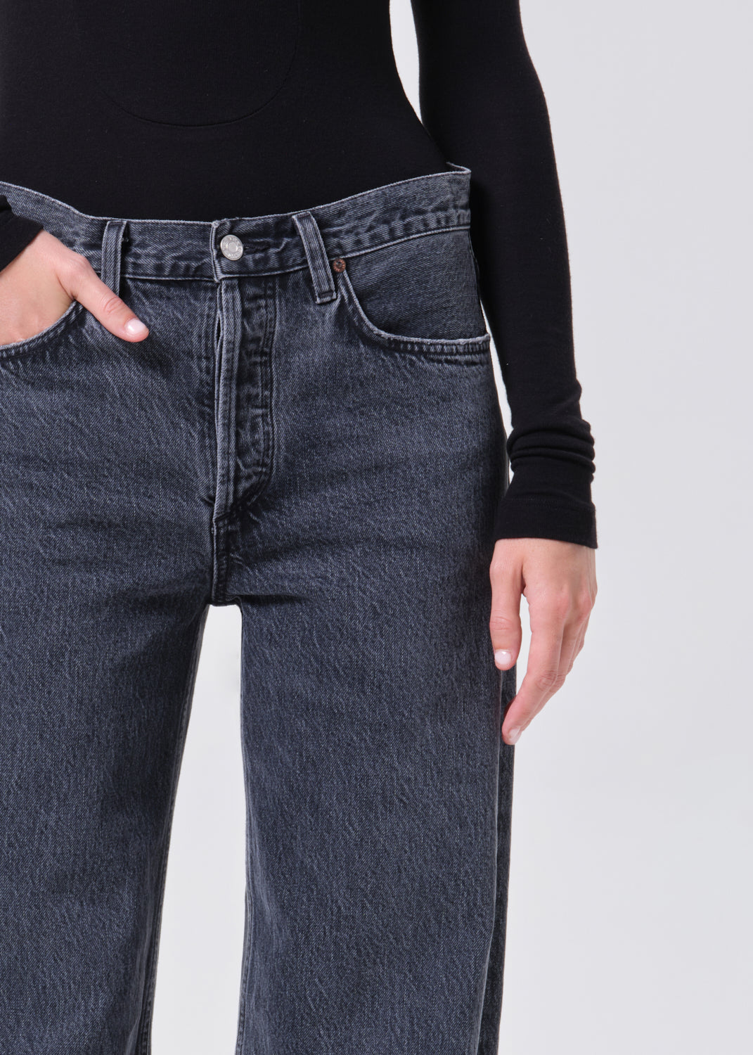 Person wearing dark blue jeans and a black long-sleeve shirt on a light gray background