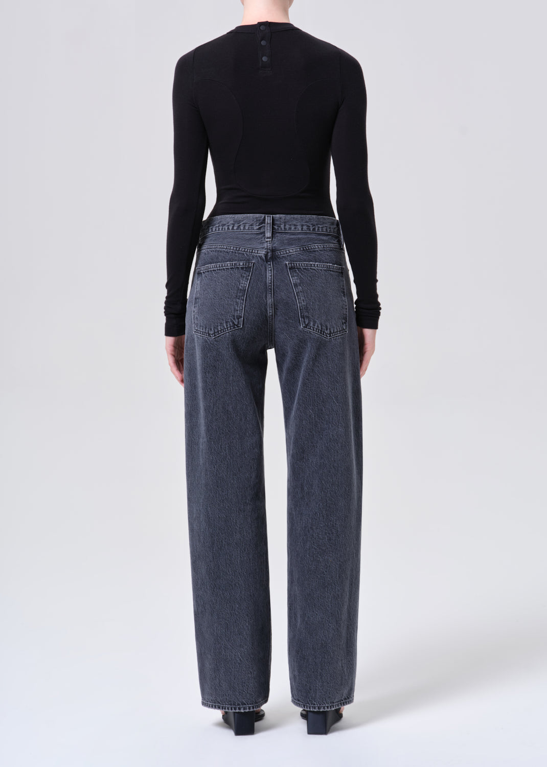 Person wearing black long-sleeve top and blue jeans on a white background