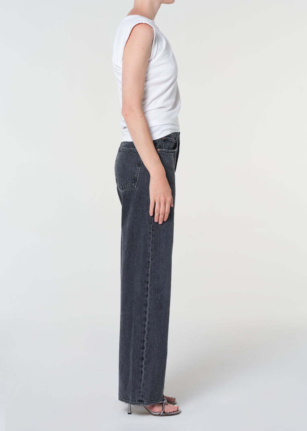 Person wearing a white sleeveless top and dark jeans on a white background