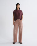 A model stands against a light gray studio background wearing a short-sleeve crewneck t-shirt in deep burgundy and high-waisted, wide-leg corduroy pants in a dusty rose pink.