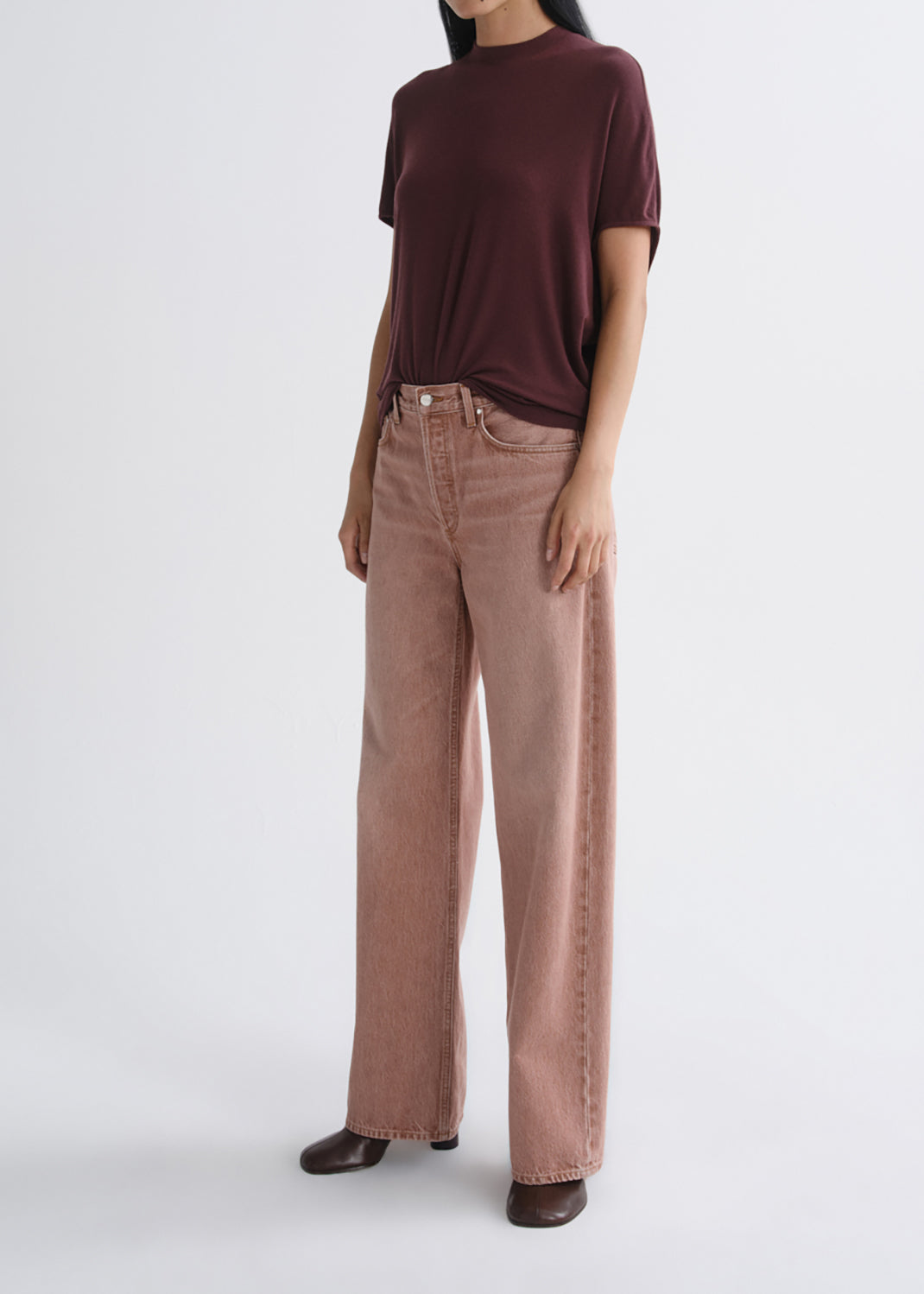 A model wearing a dark burgundy short-sleeve t-shirt and dusty rose wide-leg jeans, standing against a grey background.