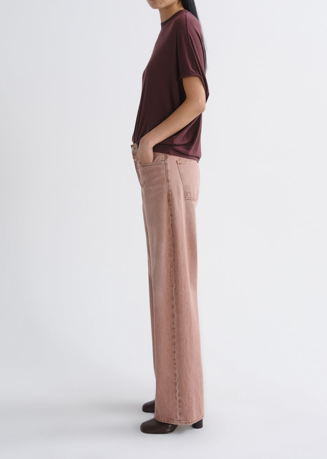 A model shown from the side wearing a dark burgundy t-shirt and dusty rose wide-leg jeans, standing against a grey background.