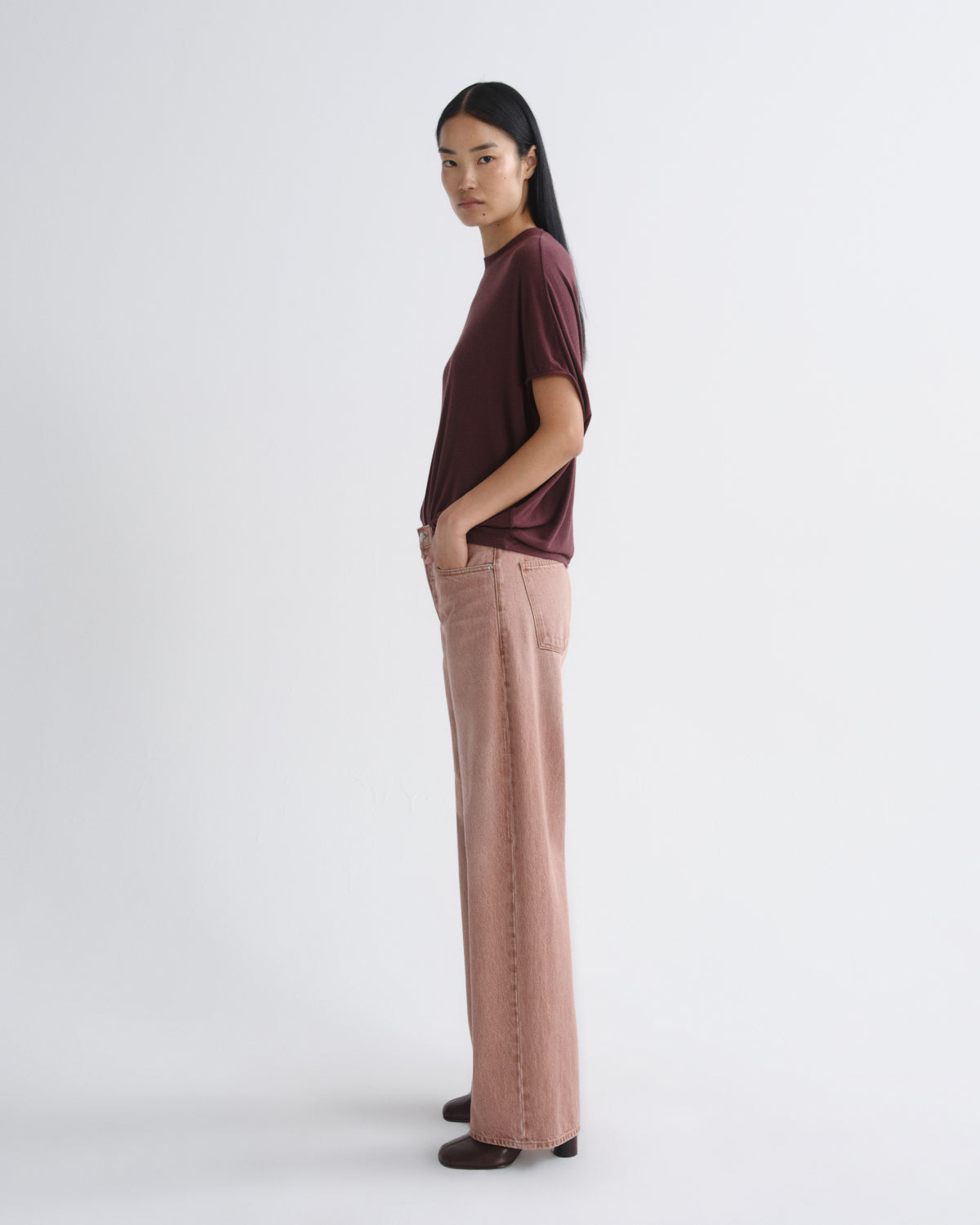 A model is shown in profile wearing a short-sleeve, dark burgundy top and wide-leg dusty rose pants against a plain light gray studio background.
