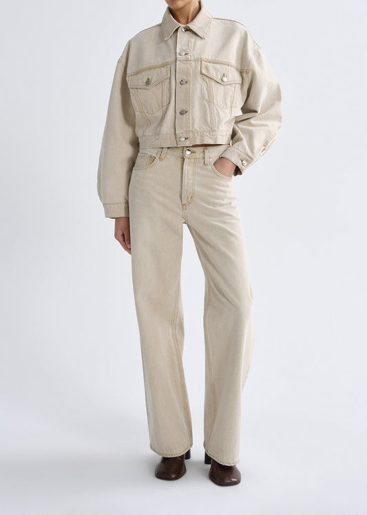 Person wearing a beige denim jacket and pants on a grey background