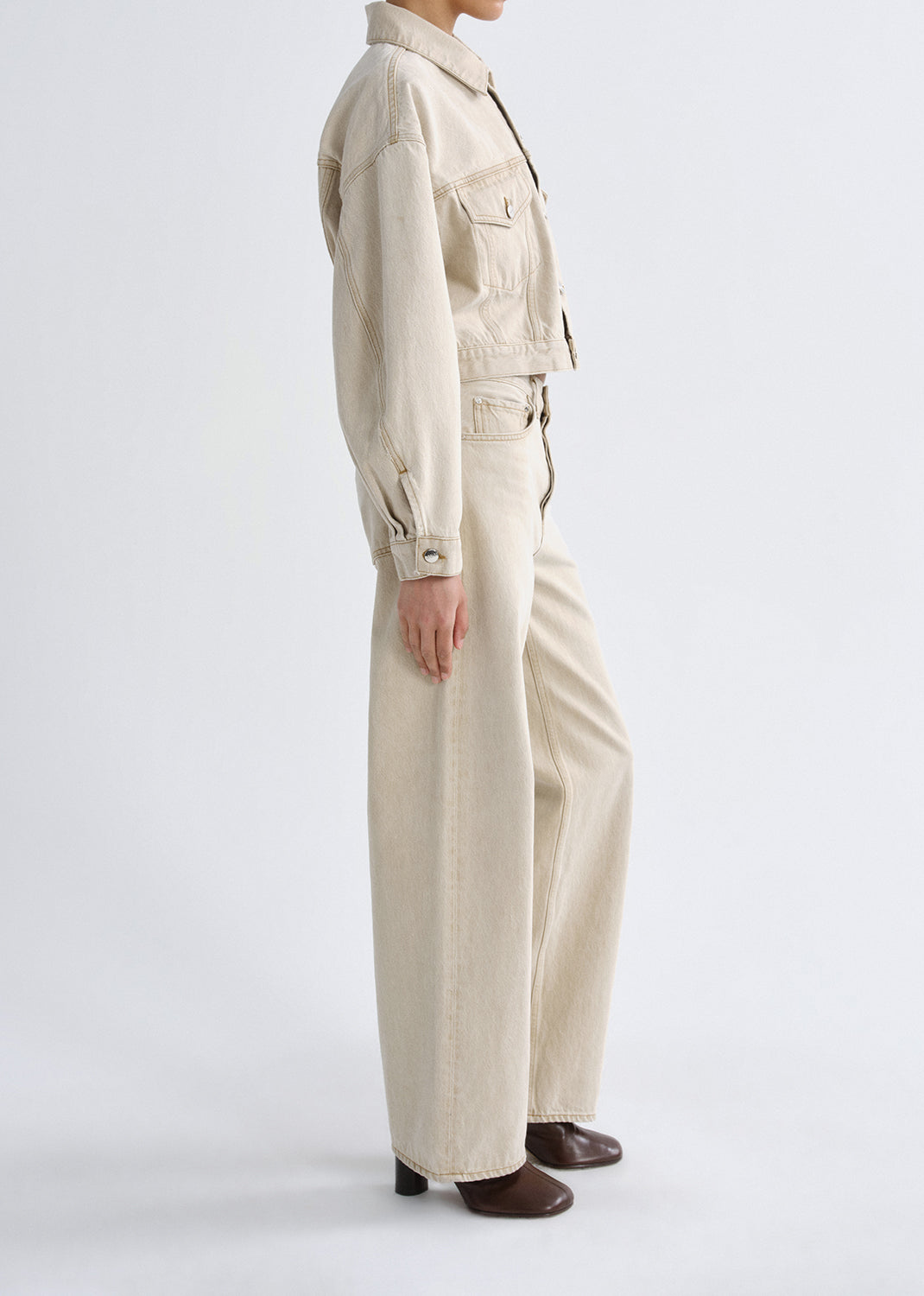 Person wearing a beige jacket and pant on a grey background