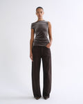 Woman wearing a brown striped sleeveless top with dark brown wide leg pants on a grey background.
