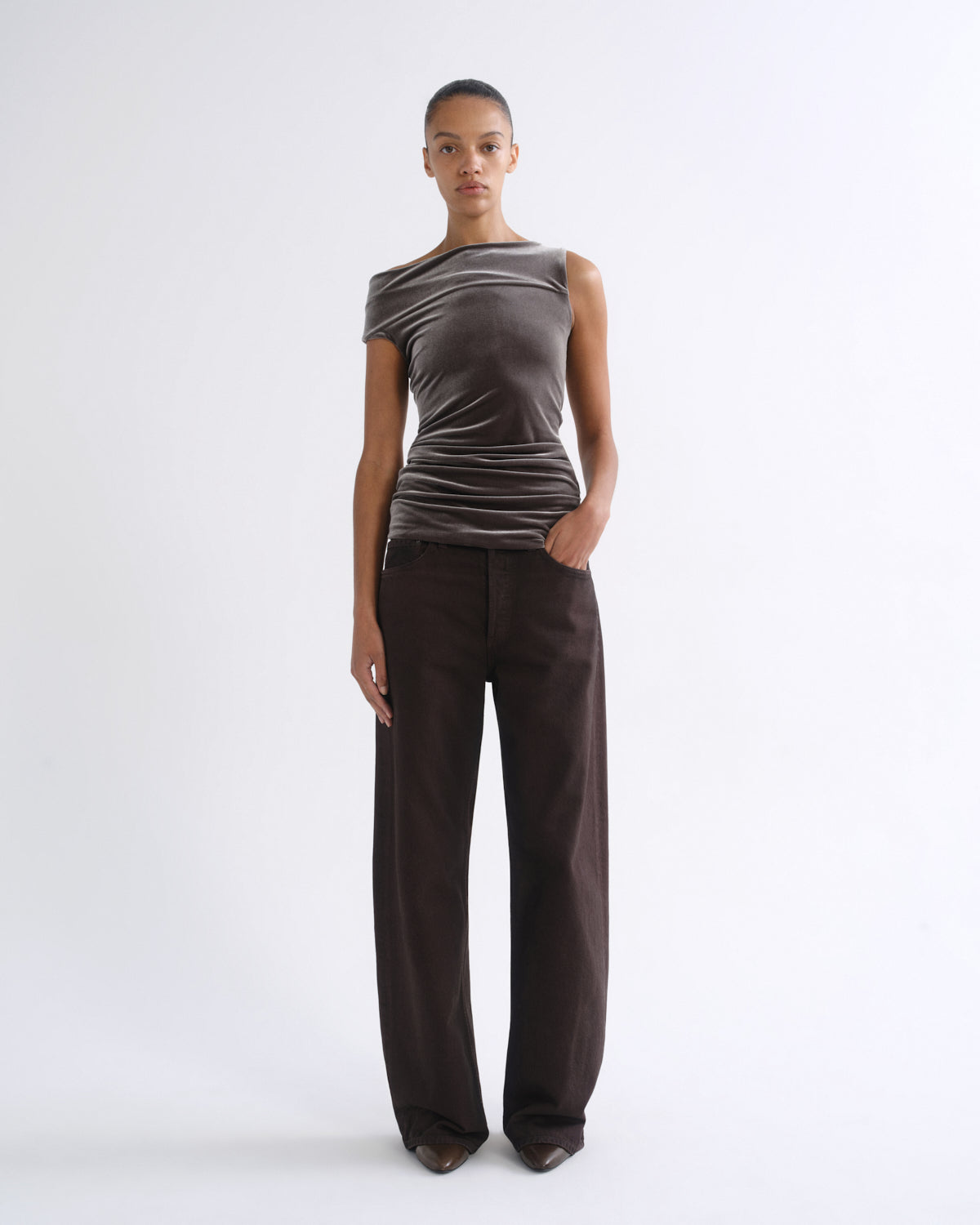 Woman wearing a brown striped sleeveless top with dark brown wide leg pants on a grey background.